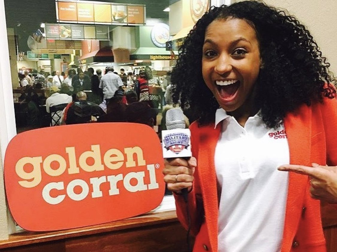 Chelsea pointing to the Golden Corral sign with a Military Appreciation Night mic